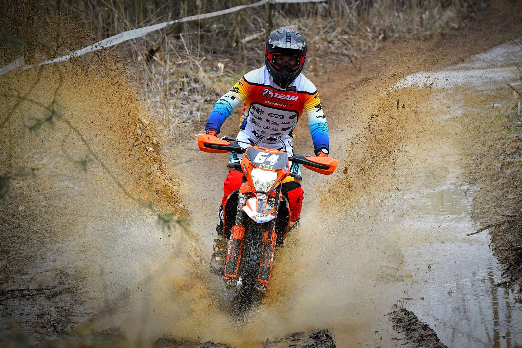 Motocross-Fahrer fährt durch Matsch mit bedrucktem Racing-Shirt