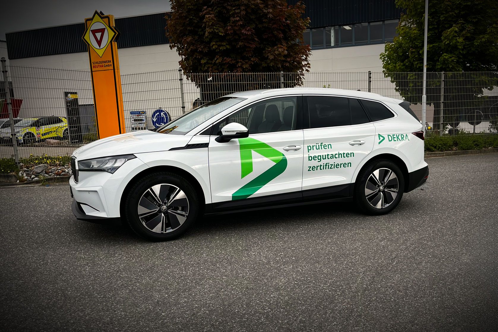 Weißes DEKRA-Fahrzeug mit grüner Markenbeschriftung „prüfen – begutachten – zertifizieren“ auf dem Gelände der Schilderwerk Beutha GmbH.