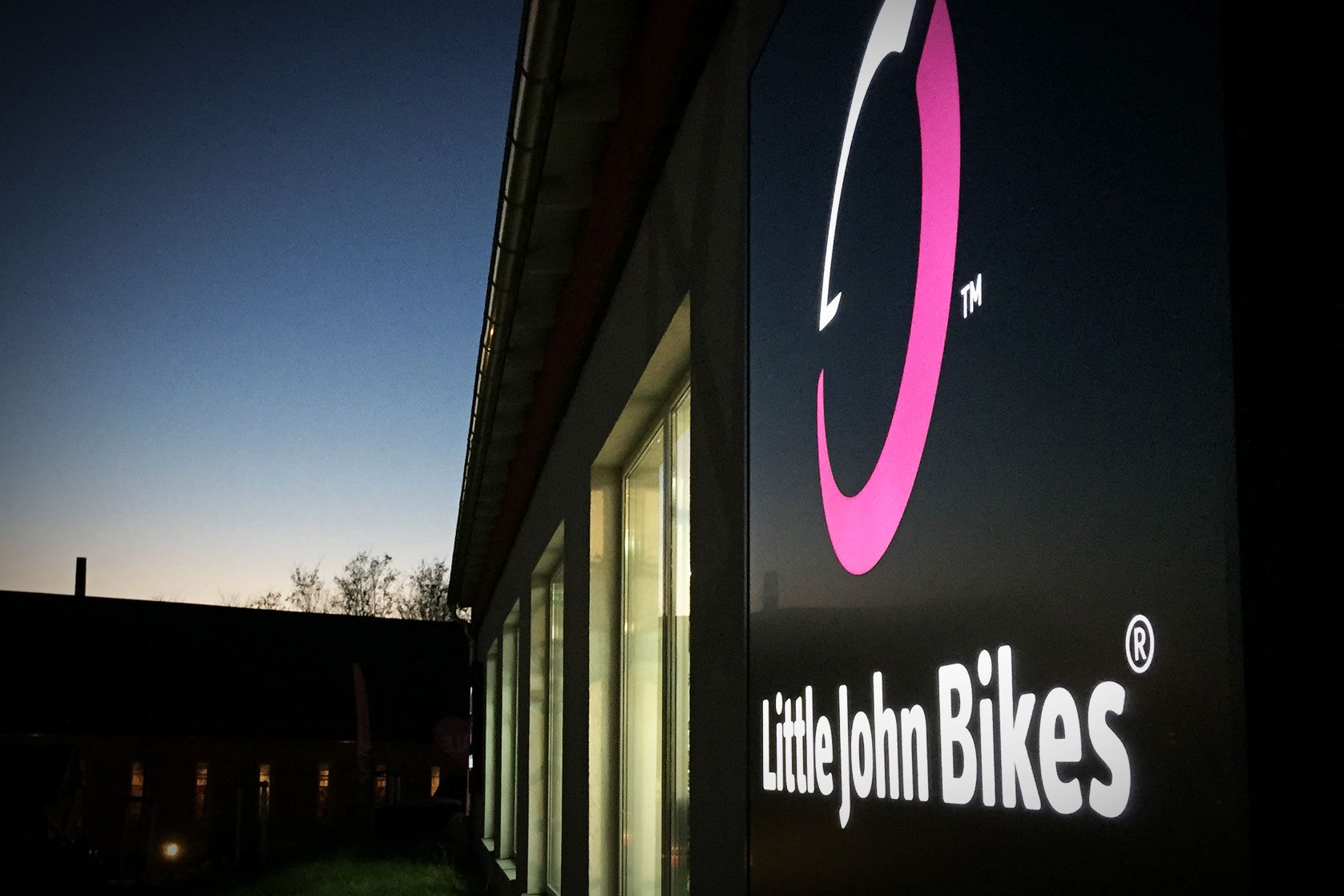 Leuchtlogo von Little John Bikes an Außenfassade bei Abenddämmerung