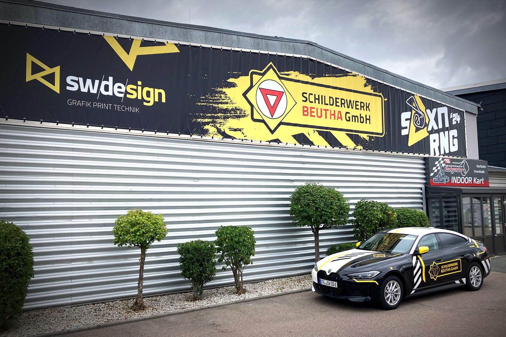 Werbebanner von sw/de/sign und Schilderwerk Beutha GmbH an Hallenfassade mit gebrandetem Fahrzeug