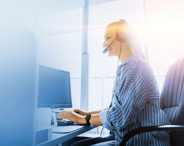 Freundliche Mitarbeiterin mit Headset im Kundendialog an einem hellen Arbeitsplatz