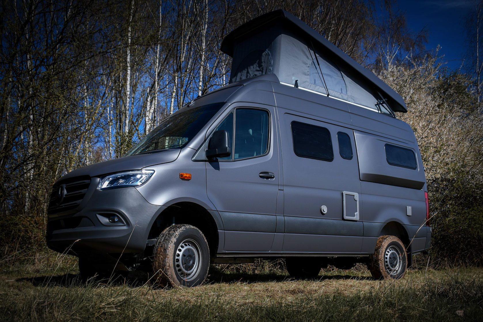 Mercedes Sprinter Camper Van mit mattem Grau-Finish und Aufstelldach in einer natürlichen Outdoor-Umgebung.