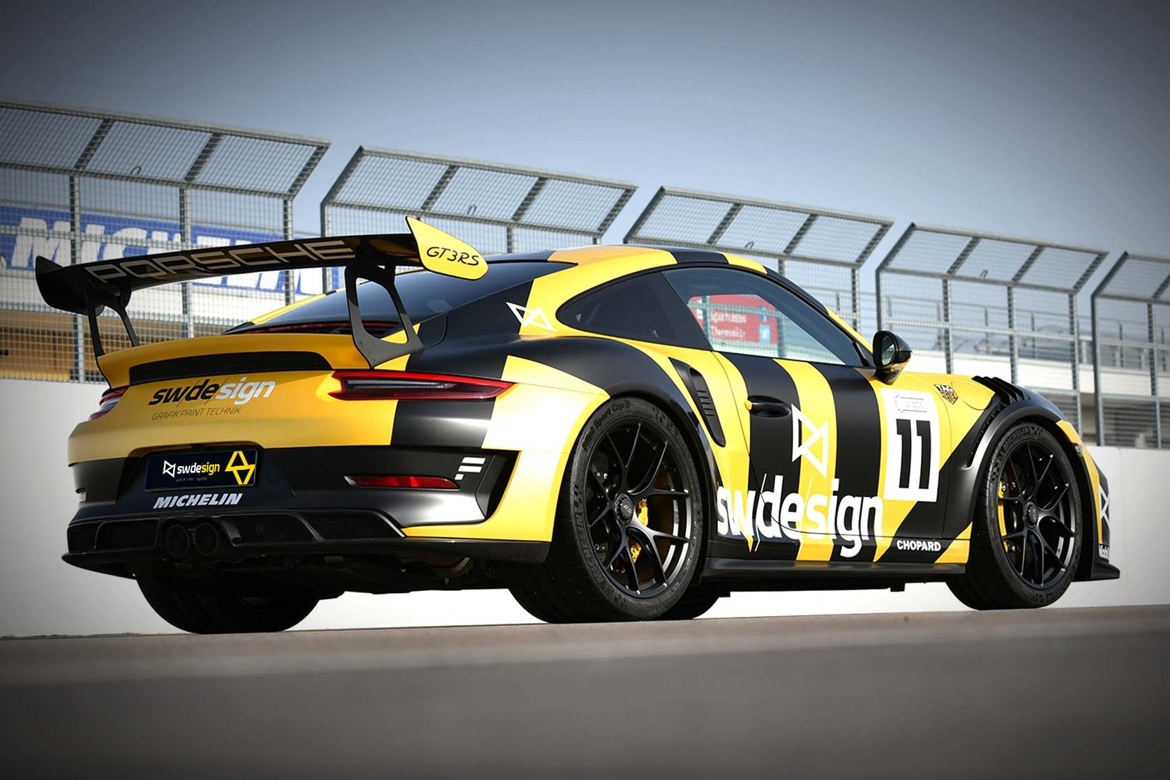 Porsche GT3 RS im schwarz-gelben sw/de/sign-Rennstrecken-Design mit großer Heckflügelbeschriftung.
