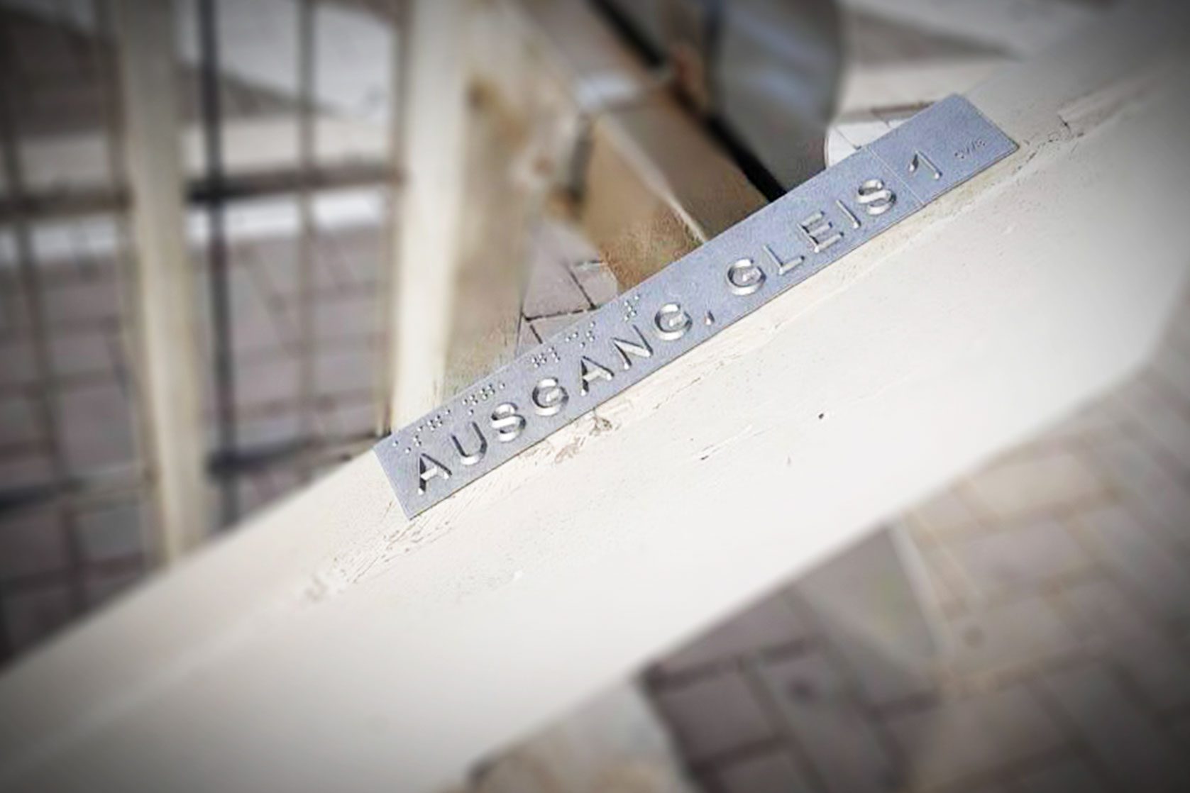 Metallplatte mit Brailleschrift und Text „Ausgang, Gleis 1“ an Geländer