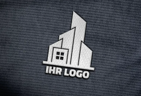 Weiße Logo-Stickerei auf grauem Textil, Nahaufnahme mit sichtbarer Fadenstruktur.