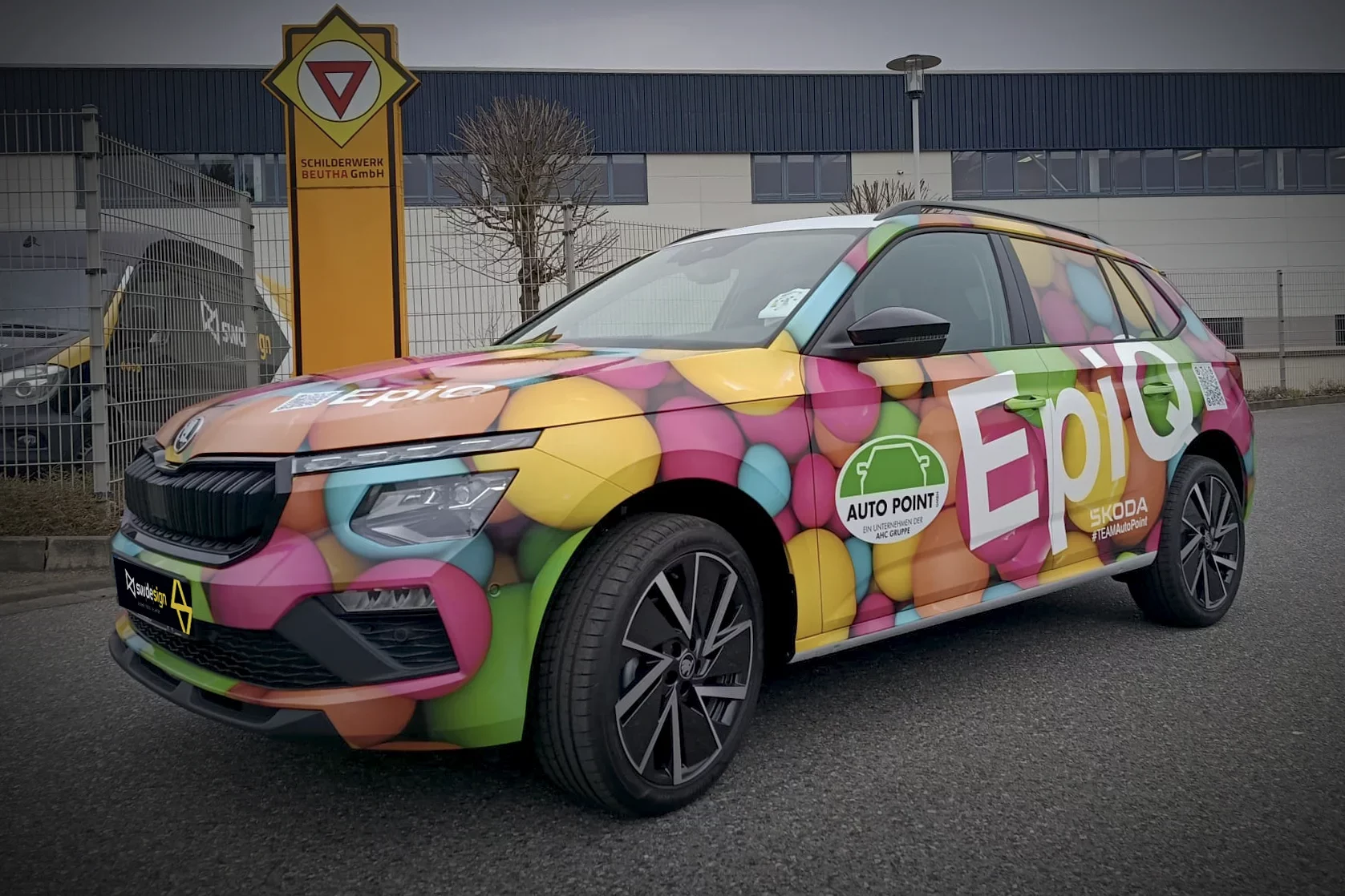 Bunt folierter Škoda SUV Kamiq mit großflächiger Werbegrafik, Logo-Elementen und auffälligem Fahrzeugdesign auf einem Parkplatz.
