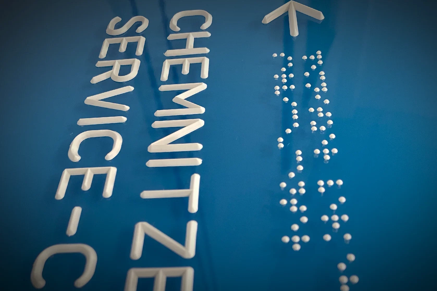 Taktile Beschilderung mit Brailleschrift und erhabener Schrift auf blauem Hintergrund zur barrierefreien Orientierung in öffentlichen Gebäuden.