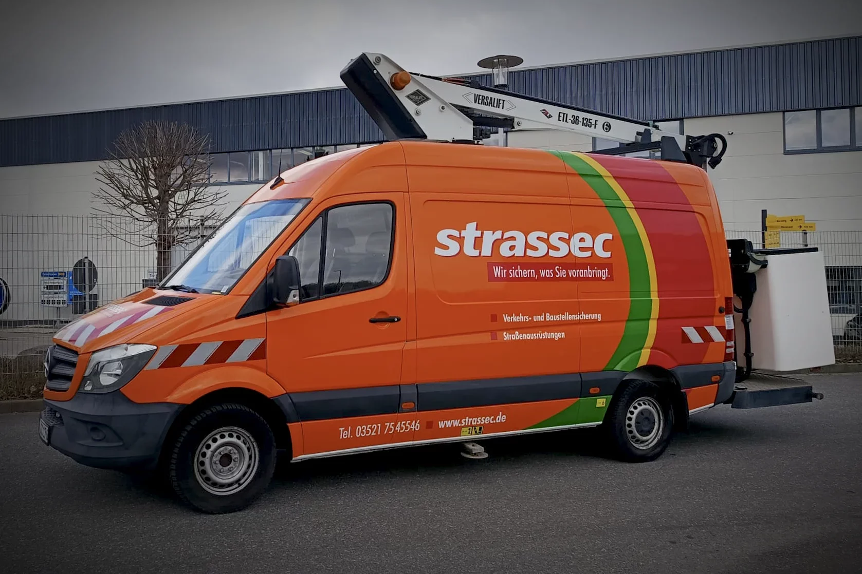 Orangefarbenes Servicefahrzeug mit Hubarbeitsbühne und professioneller Fahrzeugfolierung für Strassec aus Meißen.